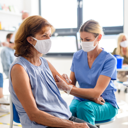 Eine ältere Dame wird von einer Ärztin geimpft - beide tragen eine Maske