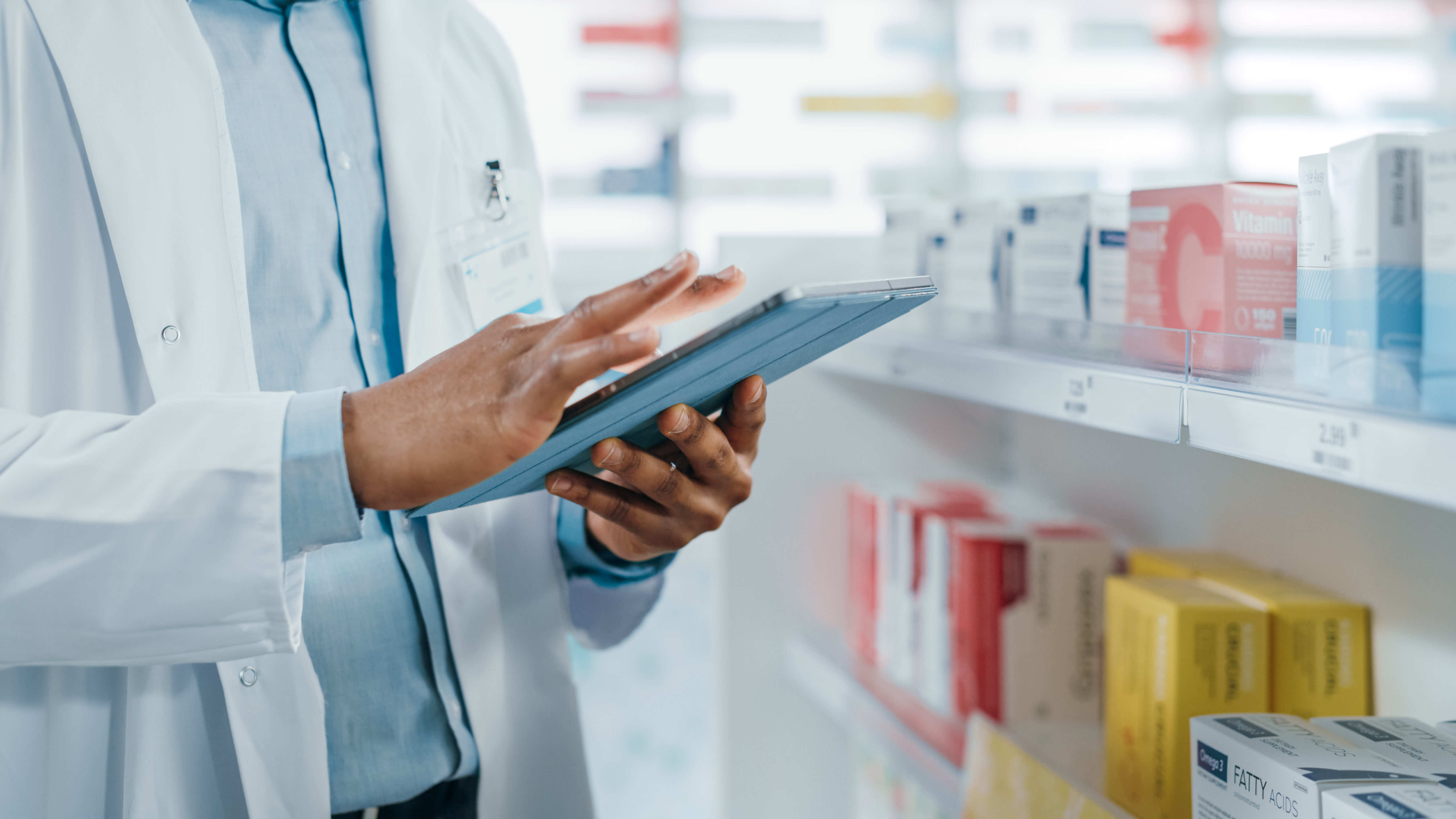 Apotheker steht vor einem Regal mit Medikamenten mit einem Tablet in der Hand