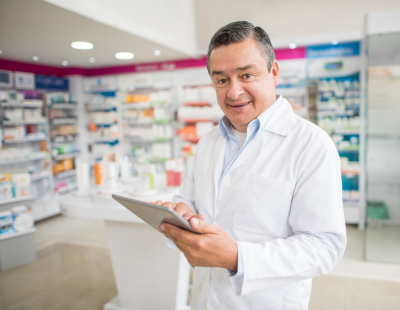 Apotheker steht in einer Apotheke mit einem Tablet in der Hand